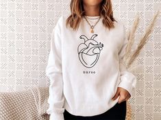 a woman standing in front of a wall wearing a white sweatshirt with an image of a heart on it