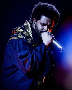 a man holding a microphone in his right hand and wearing a blue jacket on stage