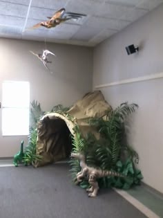 an indoor play area with fake dinosaurs and trees in the corner, including a cave