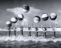 four women in bathing suits are playing with large beach balls on the water's edge