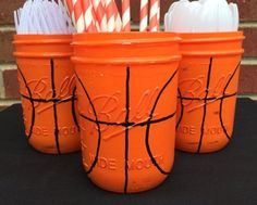 three orange mason jars with paper straws in them and one has a basketball painted on it