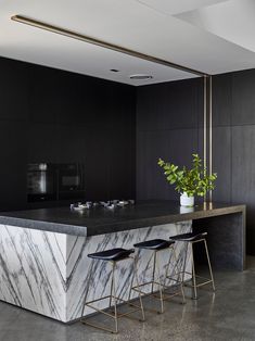 a kitchen with marble counter tops and stools next to a plant in a vase