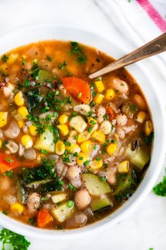 a white bowl filled with vegetable soup on top of a table next to parsley