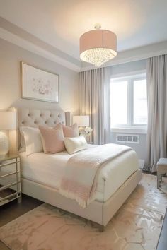 a white bed sitting in a bedroom next to two lamps and a chandelier