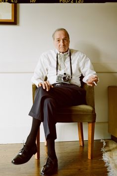 an old man sitting in a chair with a camera on his lap and wearing a tie