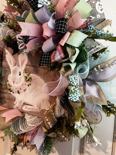 a wreath with a bunny on it hanging from the front door, decorated with ribbons and bows