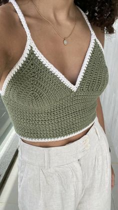 a woman wearing a green and white crochet crop top standing in front of a window