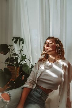 a woman sitting on the floor next to a potted plant