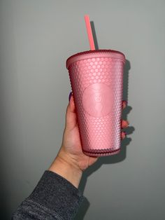 a person holding a pink cup with a straw in it's hand, against a gray wall