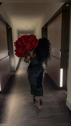 a woman walking down a hallway with red roses in her hand