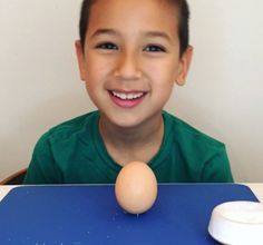 a young boy sitting at a table with an egg in front of him