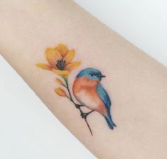 a small blue bird sitting on top of a flower next to a yellow flower tattoo