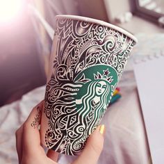 a woman's hand holding up a starbucks cup with intricate designs on the side