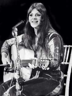 a woman sitting in front of a microphone while holding a guitar and singing into a microphone