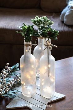 two glass bottles with christmas lights in them on a wooden table next to a couch