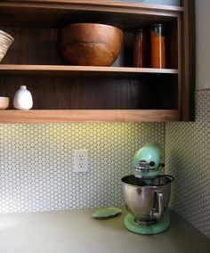 a green mixer sitting on top of a counter next to a wooden bowl and shelf