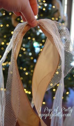 a hand is holding a pair of ballet shoes in front of a christmas tree