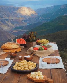 a wooden table topped with lots of food on top of a mountain side covered in watermelon