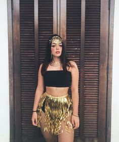 a woman standing in front of a wooden door wearing a gold skirt and headpiece