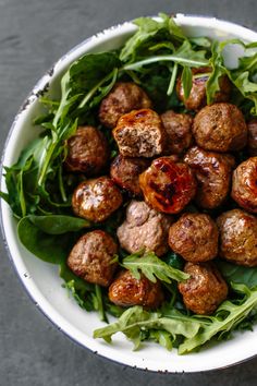 a bowl filled with meatballs and greens on top of a gray countertop next to a fork