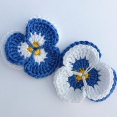 three crocheted flowers on a white surface with blue and yellow centers, one is in the shape of a flower