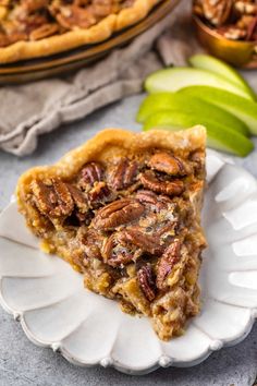 a slice of pecan pie on a white plate with an apple in the background