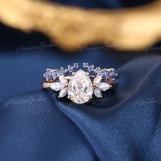 a diamond ring with blue and white stones on it's side sitting on top of a blue cloth