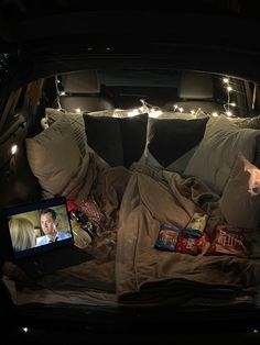 the back of a car with pillows and blankets on it's bed, lights in the background