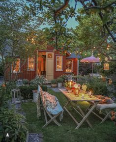 an outdoor table and chairs in front of a small red shed with lights on it