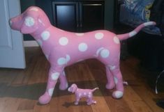 a pink and white polka dot dog statue next to a toy poodle on the floor