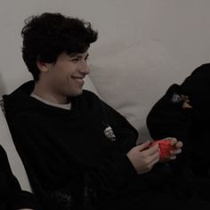 two people sitting on a couch and one is holding a nintendo wii game controller in his hand