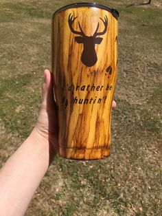 a person holding up a wooden cup with a deer head on the side and words underneath it