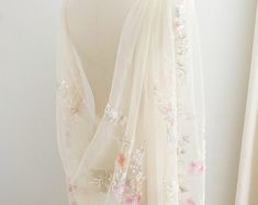 a white scarf with flowers on it hanging from a mannequin's head