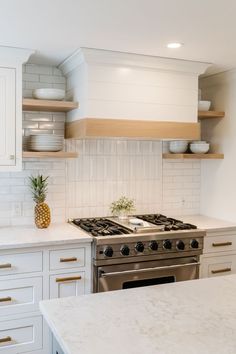 a kitchen with white cabinets and marble counter tops, pineapple vase on the stove