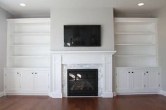 an empty living room with white bookcases and a television mounted above the fireplace