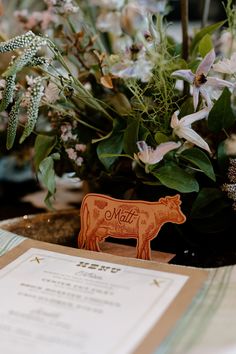 a wooden cow standing next to a menu on a table with flowers in the background