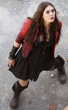 a woman in black dress and boots standing on concrete with her hands behind her back