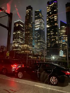 two cars parked on the side of the road in front of tall buildings at night