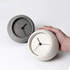 a hand is holding an alarm clock in front of the other one, which appears to be made out of concrete