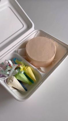 a plastic container filled with food on top of a white table next to a cup