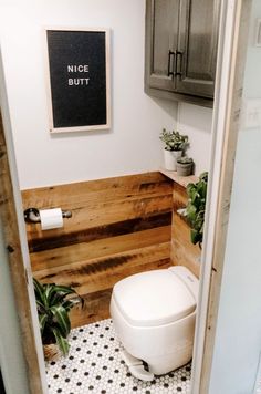 a white toilet sitting inside of a bathroom next to a wooden wall and planters