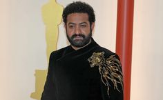 a man with a beard wearing a black shirt and standing in front of an oscar statue