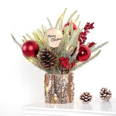 a christmas arrangement with pine cones, berries and other holiday decorations in a tinsel vase