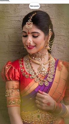 a woman in an orange and pink sari with gold jewelry on her neck, standing next to a brick wall