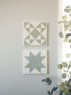 two green and white quilts hanging on the wall next to a potted plant