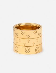 three gold rings with smiley faces and hearts on the sides, set against a white background