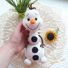 a crocheted snowman sitting on top of a doily next to a potted plant