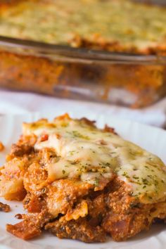 a white plate topped with lasagna covered in sauce and cheese next to a casserole dish