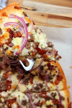 a slice of pizza with meat, onions and cheese is being held up by a spatula