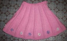 a pink knitted skirt with flowers on the bottom and side, sitting on a bed